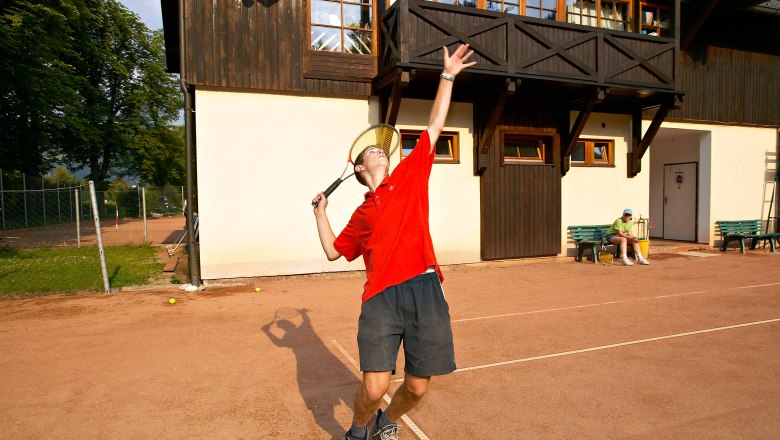 Person playing tennis in front of a building.