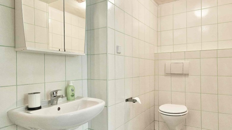 Modern bathroom with white tiles, washbasin, mirror and toilet.