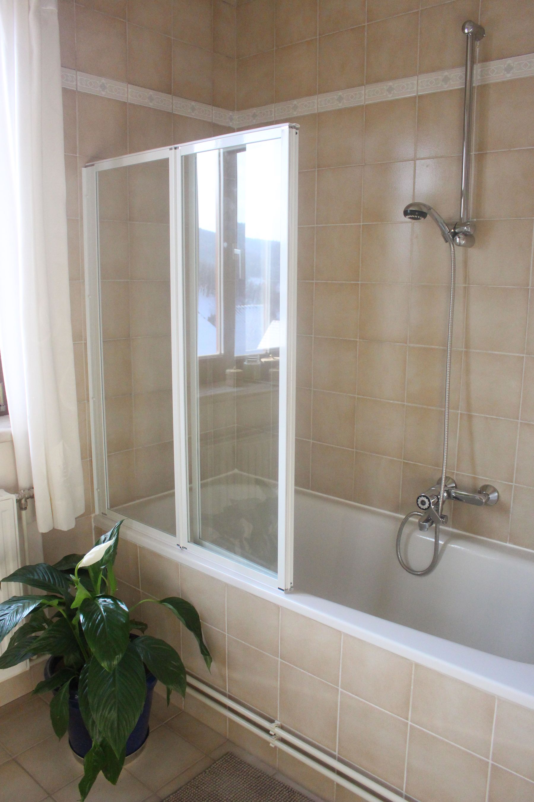 Ein Badezimmer mit einer Badewanne, Duschvorhang, Fliesen und einer Pflanze.