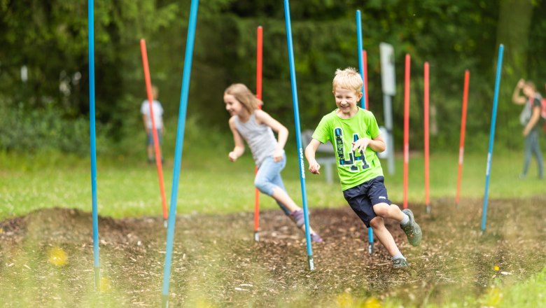 Kinder laufen durch einen Parcours mit bunten Stangen im Motorikpark St. Corona.