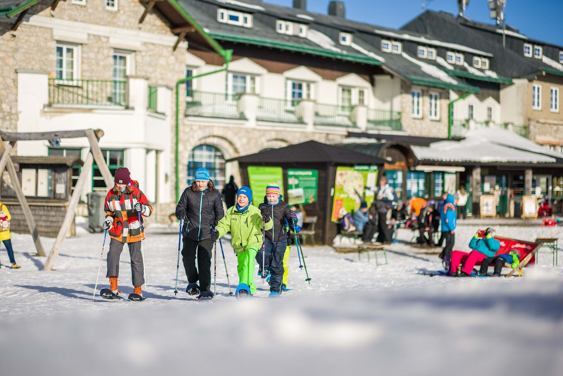 In der glitzernden Winterlandschaft genießen Familien das Schneeschuhwandern und erleben die frische Bergluft. Die schneebedeckten Hügel und die strahlende Sonne schaffen eine einladende Atmosphäre für Abenteuer in der Natur.