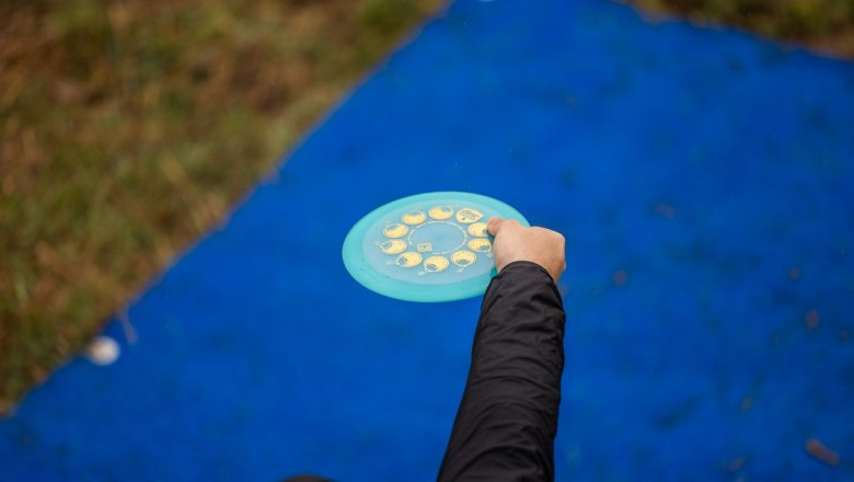 Person hält eine Discgolf-Scheibe über einer blauen Matte, die Hand zum Wurf ausgestreckt