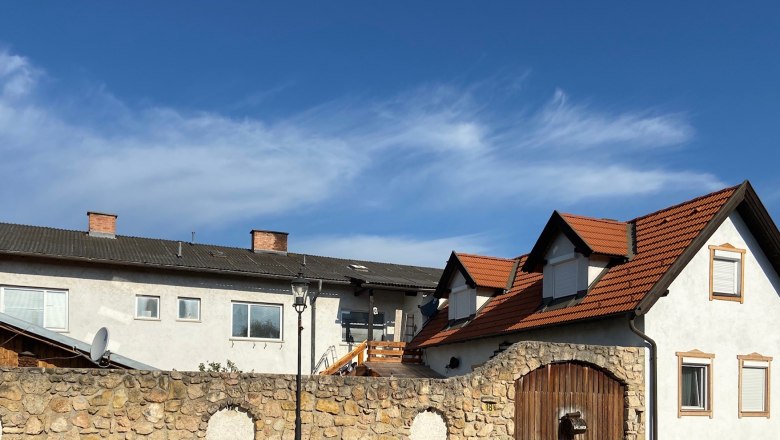 Ferienappartement Valenta, © Wiener Alpen Ein Gebäude mit roten Ziegeldächern und einer Steinmauer im Vordergrund unter blauem Himmel.