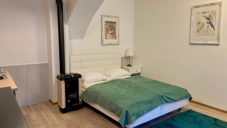 Ein gemütliches Schlafzimmer mit einem weißen Bett, grüner Decke, Teppich und zwei Bildern an der Wand.