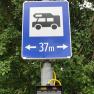 Ein blaues Verkehrsschild mit einem Wohnmobil-Symbol und der Aufschrift '37 m' mit Pfeilen nach links und rechts.