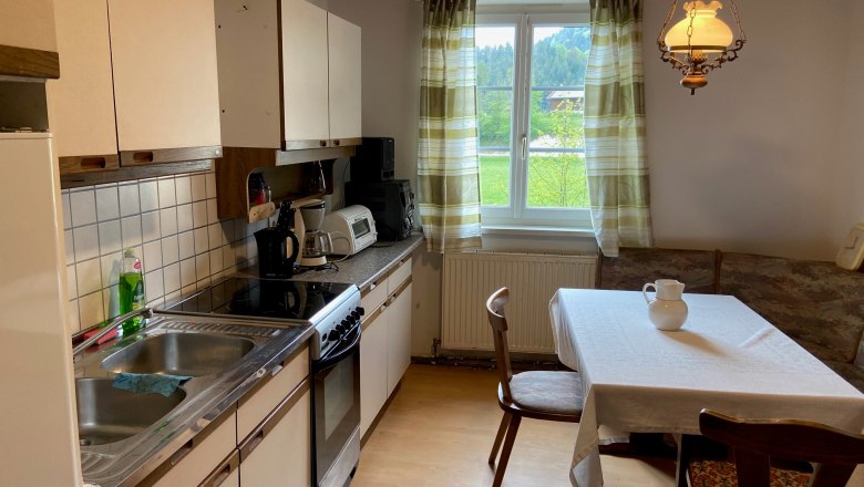 Küche mit Esstisch, Stühlen, Spüle, Herd und Fenster mit Vorhängen.