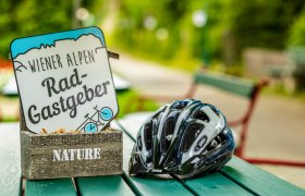 Wiener Alpen Rad-Gastgeber Plakette liegt mit Radhelm auf türkisem Tisch 