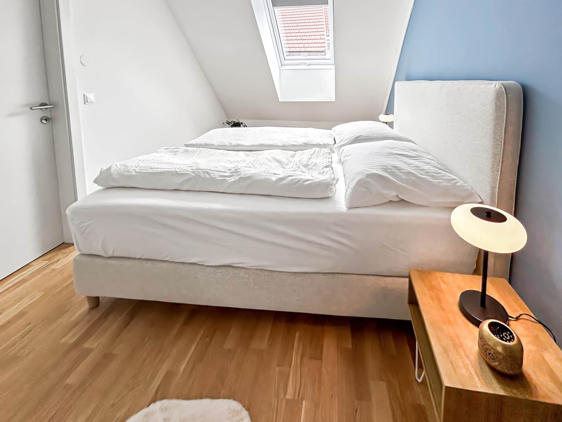 Bedroom with sloping ceiling and window. Bedside cabinet with lamp.