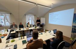 Mehrere Workshop Teilnehmer sitzen an Tischen, während ein Mann einen Vortrag hält.