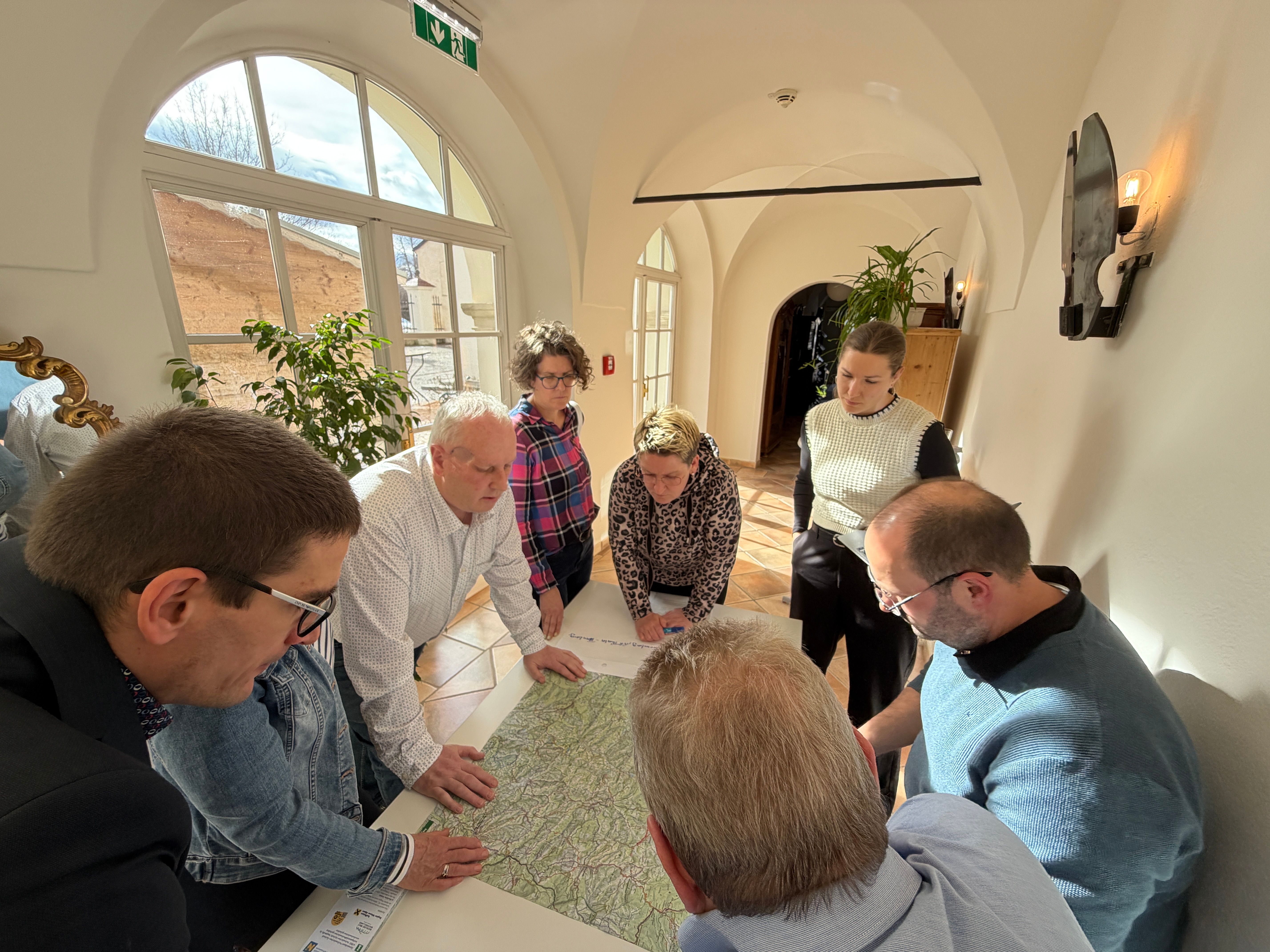 Mehrere Personen stehen über eine Wanderkarte gebeugt an einem Tisch.