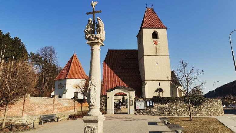 Pfarrkirche Unter-Aspang mit Säule im Vordergrund und blauem Himmel.