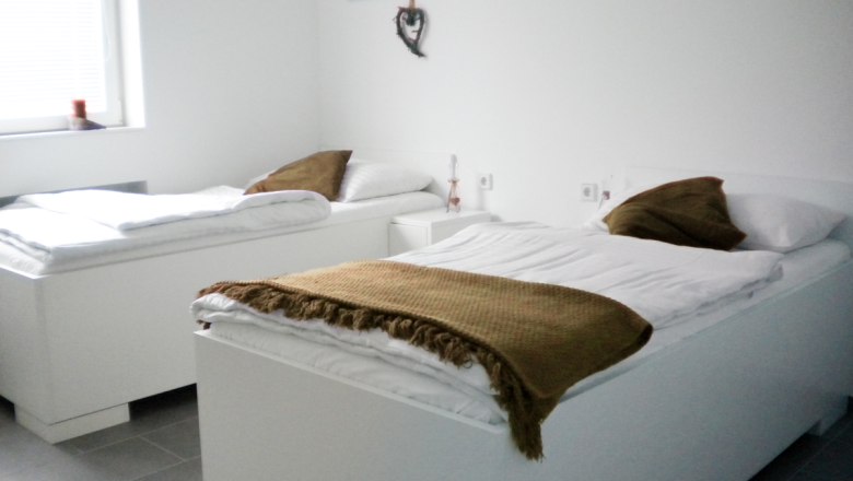 Arbeiterquartier UHL, © Arbeiterquartier UHL Zwei weiße Betten in einem hellen Raum mit braunen Decken und Kissen.