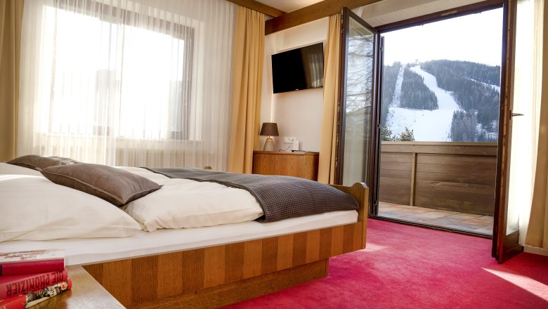 Hotel room with open balcony and view of a snow-covered ski slope.