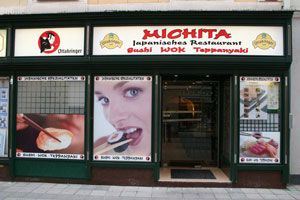 Eingang des Michita japanischen Restaurants mit großen Fenstern und Werbebildern.