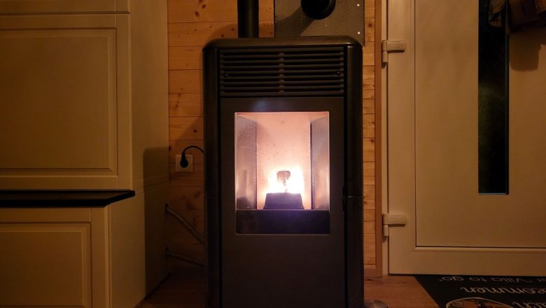 A burning pellet stove in a room with wooden walls and a door.