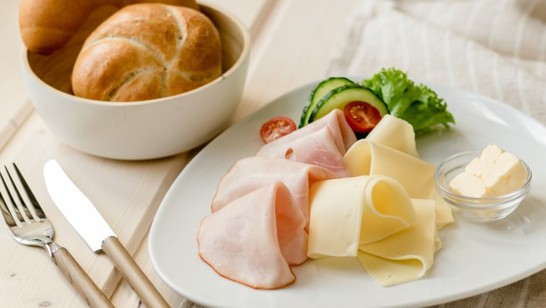 Breakfast plate with ham, cheese, gherkins, tomatoes and bread rolls.