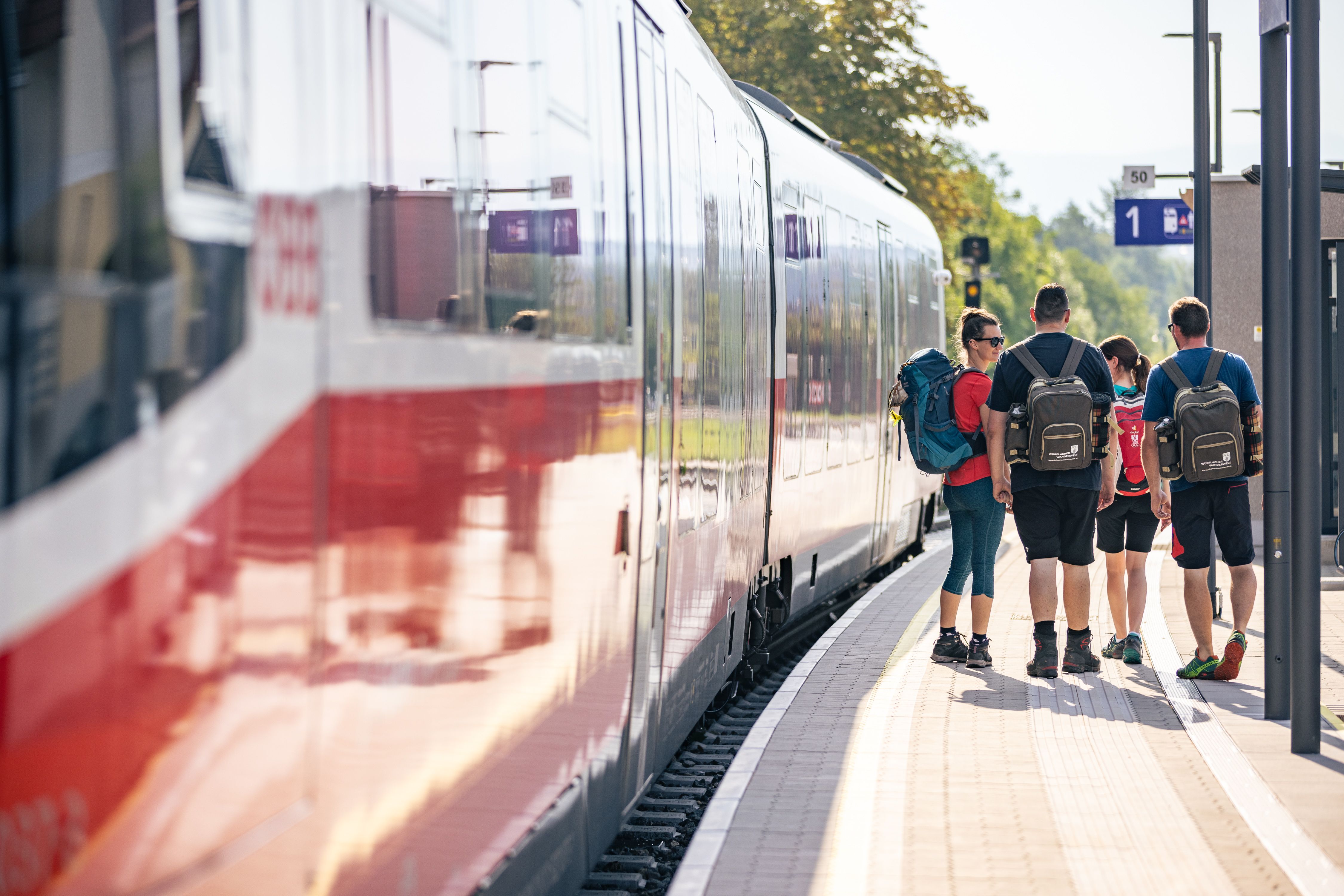 Wanderer stehen am Bahnsteig, der Zug an der Haltestelle