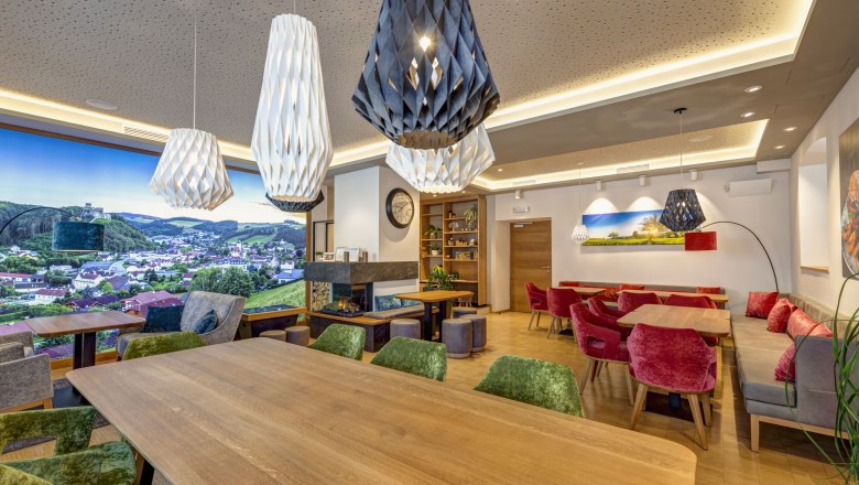 Innenansicht eines modernen Bistros mit Holztischen, bunten Stühlen und großen, dekorativen Lampen.