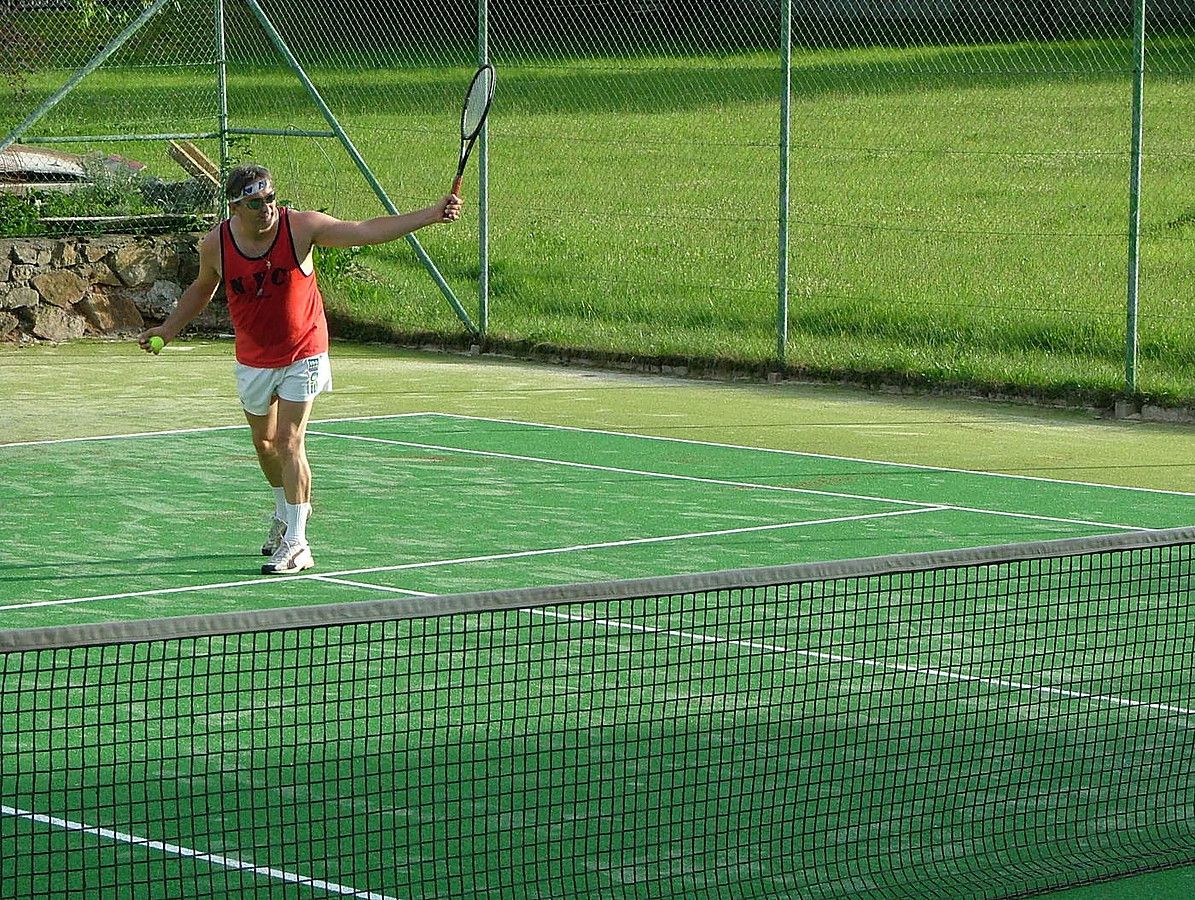 Person plays tennis on a green outdoor tennis court.