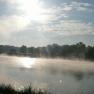A misty lake at sunrise with trees in the background.