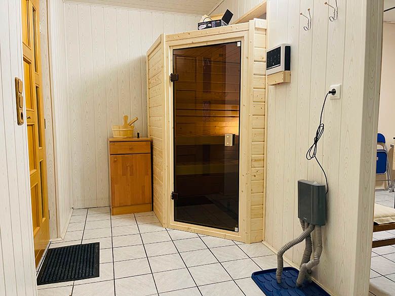 Interior view of a sauna room with wooden walls, a glass door and a small wooden cabinet.