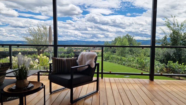 Terrasse mit Holzboden, modernen Möbeln und Blick auf eine grüne Landschaft und Berge.