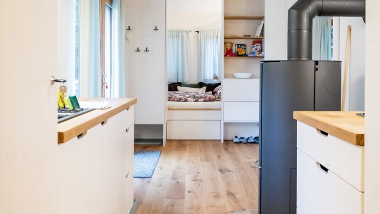 Innenansicht eines modernen, kompakten Wohnraums mit Holzfußboden, Küchenzeile und Schlafbereich.