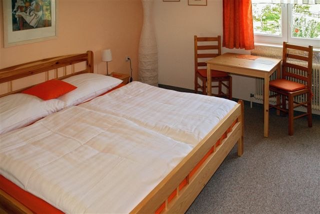 Gemütliches Gästezimmer mit Doppelbett, Holzmöbeln und einem kleinen Tisch am Fenster.