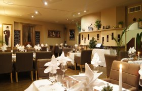 Elegantes Restaurant mit gedeckten Tischen, Kerzenlicht und dekorativen Bildern an den Wänden.