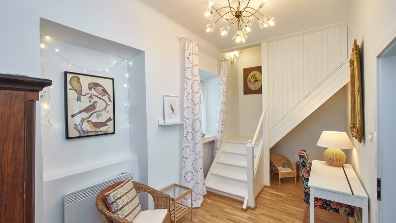 Wohnbereich mit Treppe, Rattanmöbeln und Vogelbildern an der Wand.