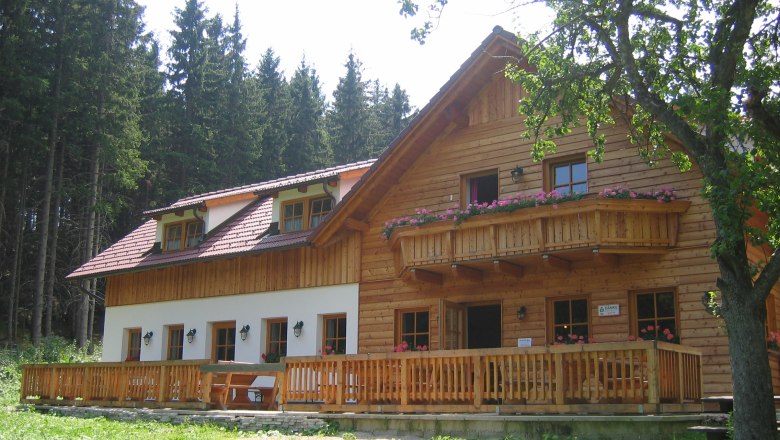 Eine rustikale Berghütte aus Holz mit Balkon und Terrasse, umgeben von Bäumen.
