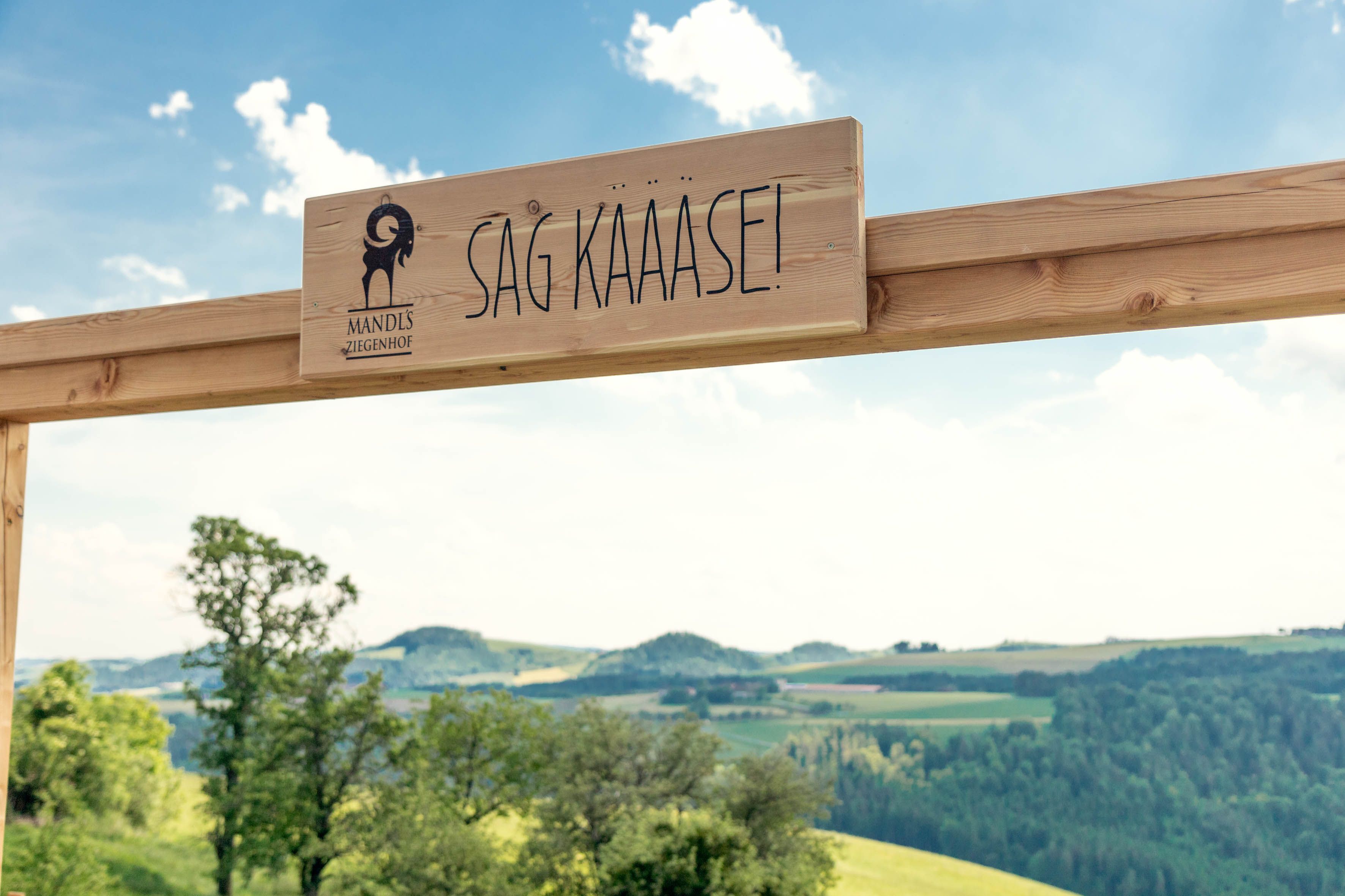 Ein Holzrahmen im Freien, im Hintergrund grüne Wiesen und Hügel.