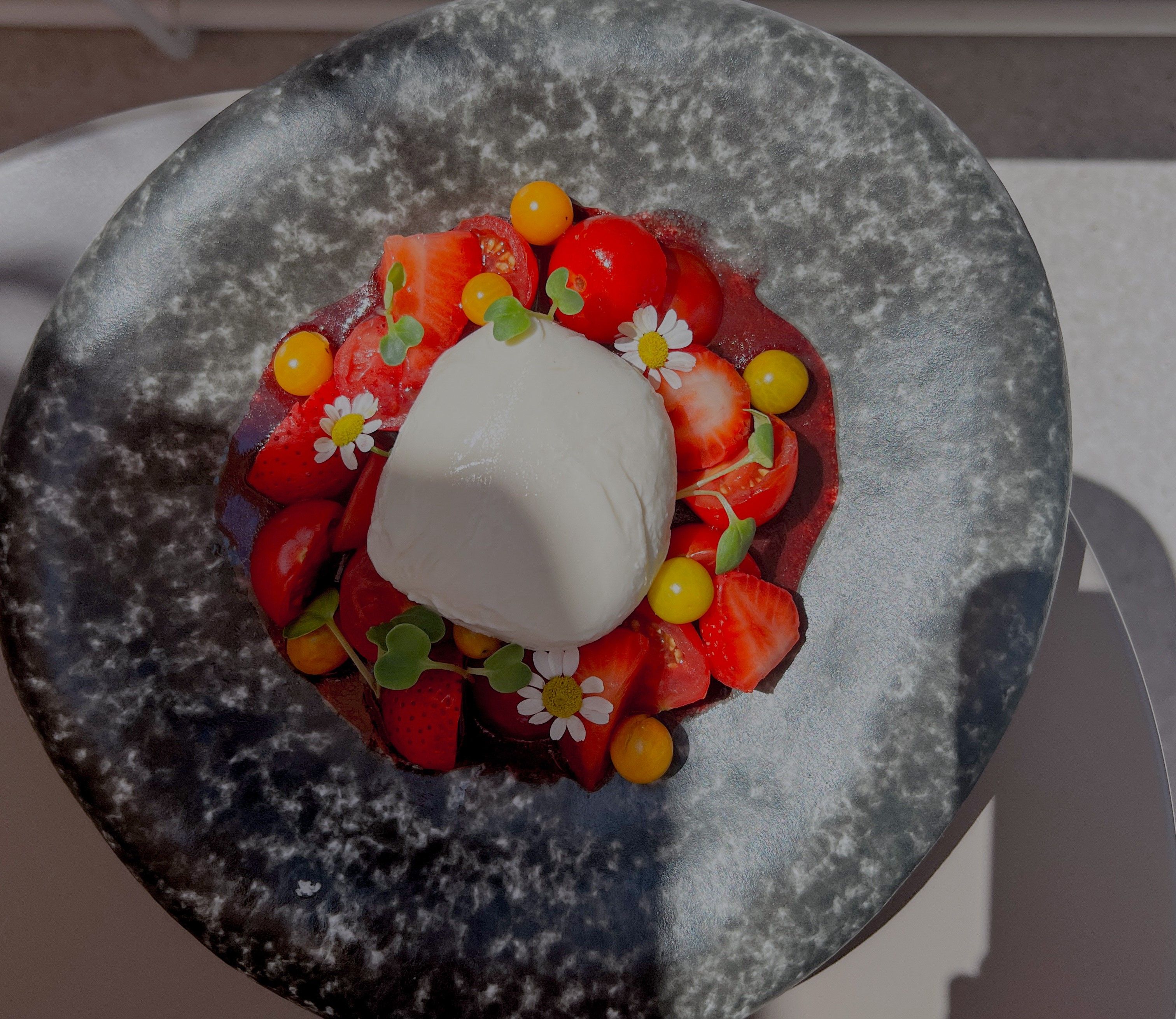 Ein Teller mit Burrata, Erdbeeren, Tomaten und essbaren Blüten.