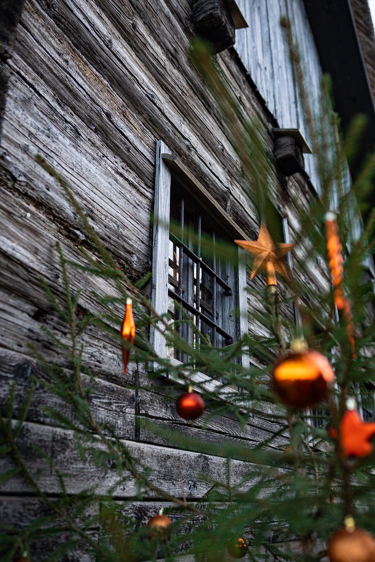 Detail einer Holzhütte mit weihnachtlich geschmücktem Tannenzweig und Kugeln.
