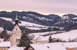 Blick auf die Wehrkirche in Bad Schönau über schneebedeckte Dächer sowie im Hintergrund auf das Schloss Krumbach.