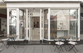 Exterior view of a café with tables and chairs on the sidewalk.