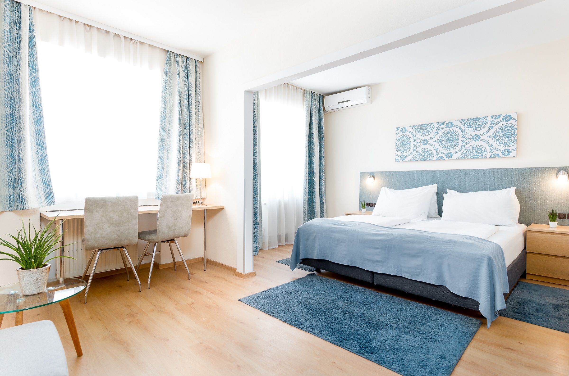 Helles, blaues Zimmer mit Doppelbett, Schreibtisch, Sitzmöglichkeiten