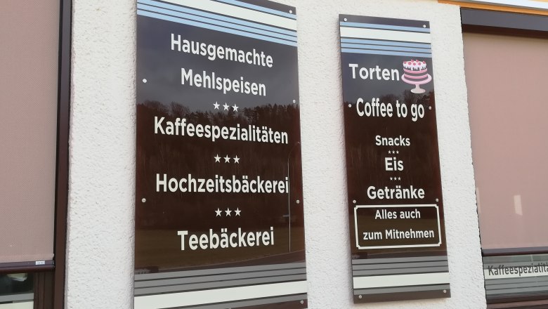 Zwei braune Schilder an der Wand mit Angeboten eines Kaffeehauses wie Mehlspeisen und Eis.