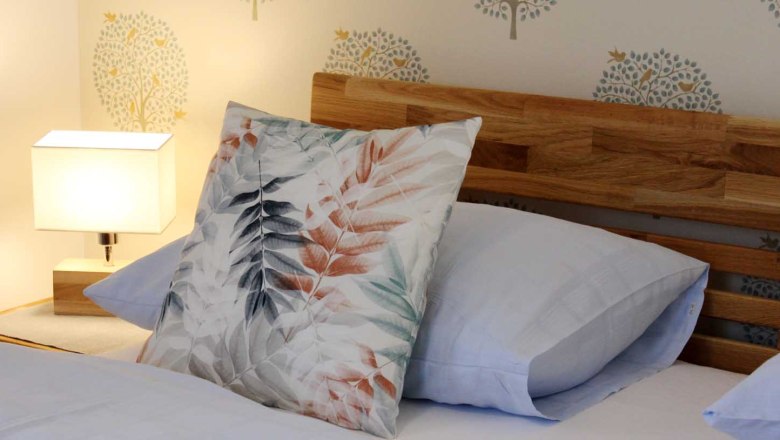 Nahaufnahme eines Bettes mit Holzkopfteil, dekorativen Kissen und Nachttischlampe.