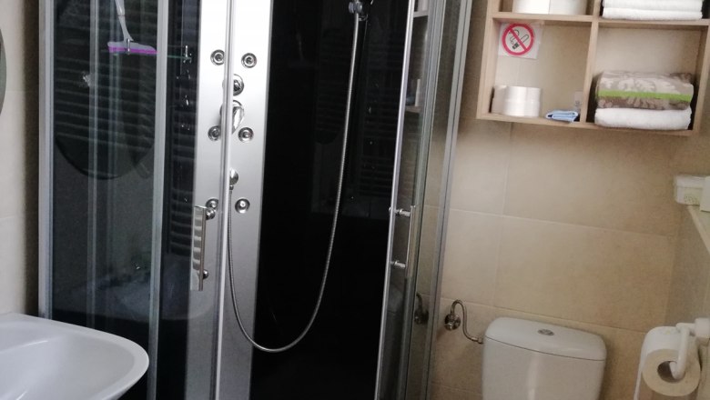 Modernes Badezimmer mit Duschkabine, Waschbecken, Toilette und Regal mit Handtüchern und Toilettenpapier.