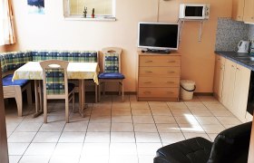 Küche mit Eckbank, Tisch, Stühlen, Fernseher, Mikrowelle und Schränken.