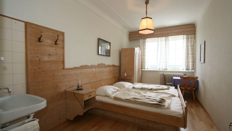 Comfortable hotel room with wooden furniture, double bed, washbasin and window with curtains.