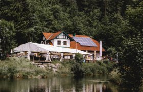 Inn with solar panels and tent on the edge of the forest, near a pond.