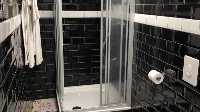 Modern bathroom with black tiled wall, colorful floor tiles, shower, towel and toilet.