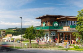 Gebäude der Eis-Greissler Welt mit Bäumen und Besuchern und Blick auf den Erlebnispark.