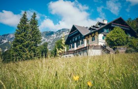 Ein traditionelles Gebäude namens Knappenhof in einer grünen Wiese vor einer Bergkulisse.