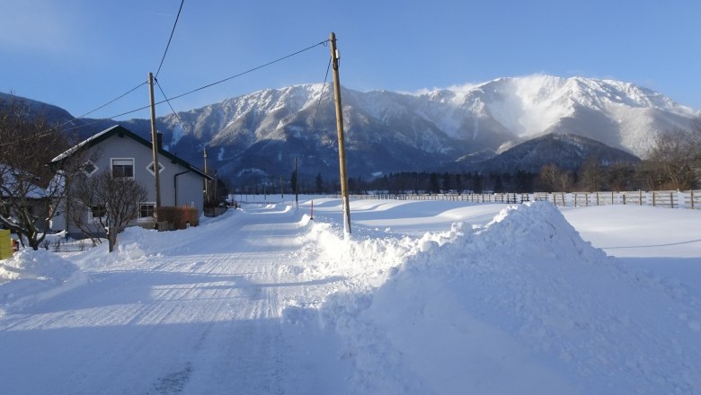 Snowy landscape with a house and mountains in the background.