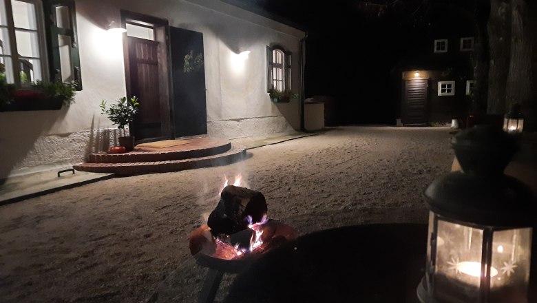 Ein beleuchteter Hof bei Nacht mit einem Feuerkorb und einer Laterne im Vordergrund.