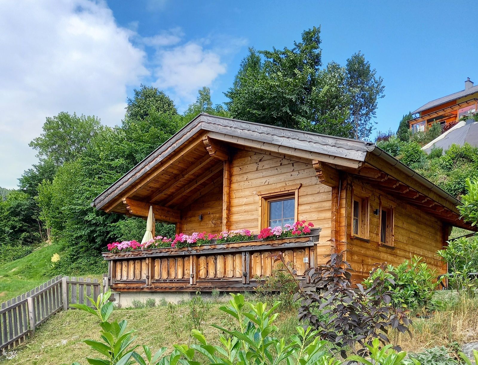 Holzhütte mit Blumen auf der Veranda in einer grünen Umgebung.