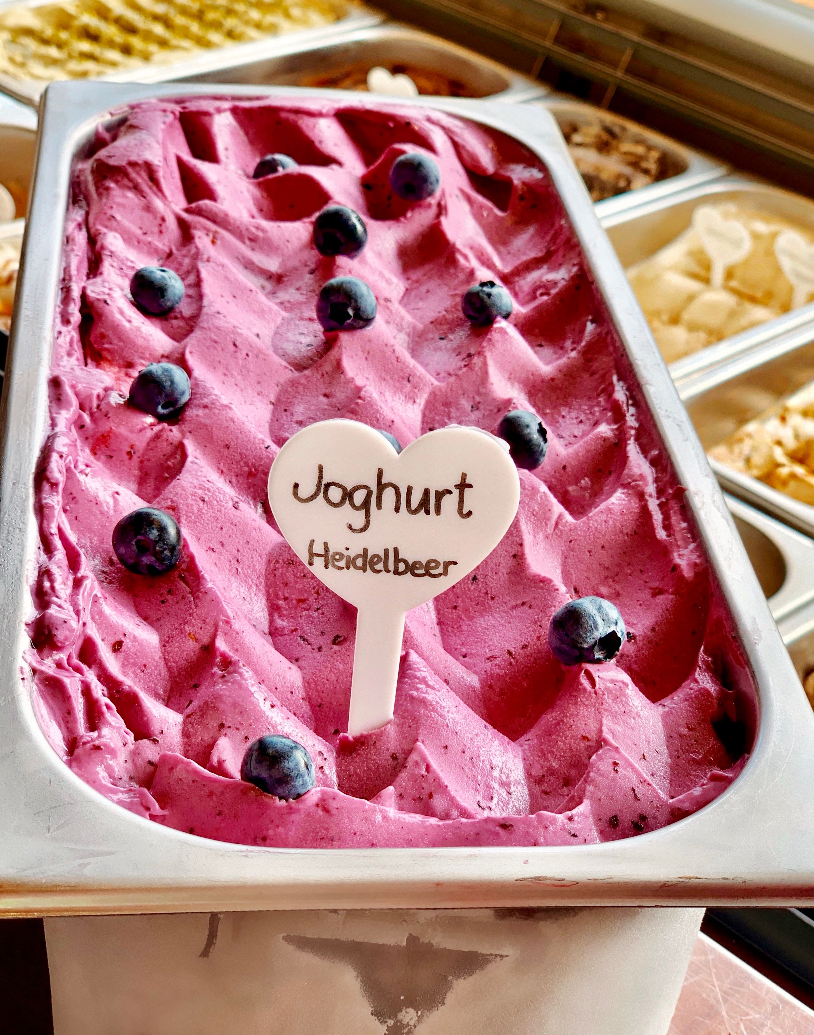 Ein Eisbehälter aus Metall mit Joghurt-Heidelbeer-Eis, dekoriert mit frischen Heidelbeeren.